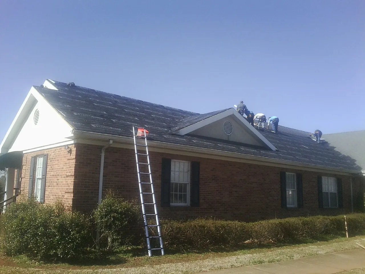 Crew tearing shingles off a brick ranch roof with a ladder set — Metal Roof Repair work by our crew in Fielding
