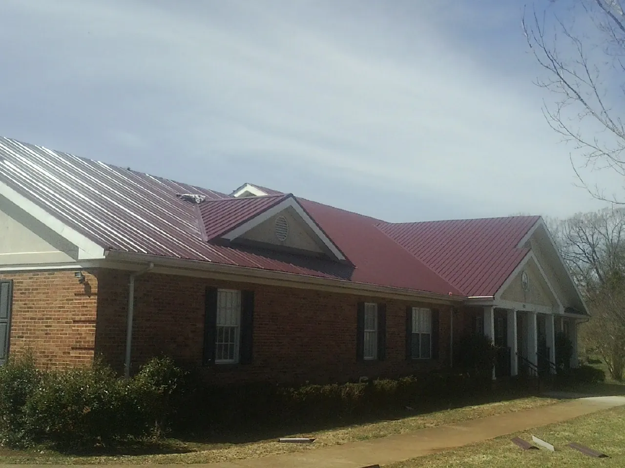 Red metal roof with gabled entries on a long brick building, from a Hail Damage Roof Repair job in Fielding