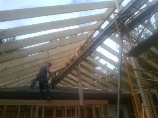 Rafters going up over a new addition with a worker on the wall in Fielding