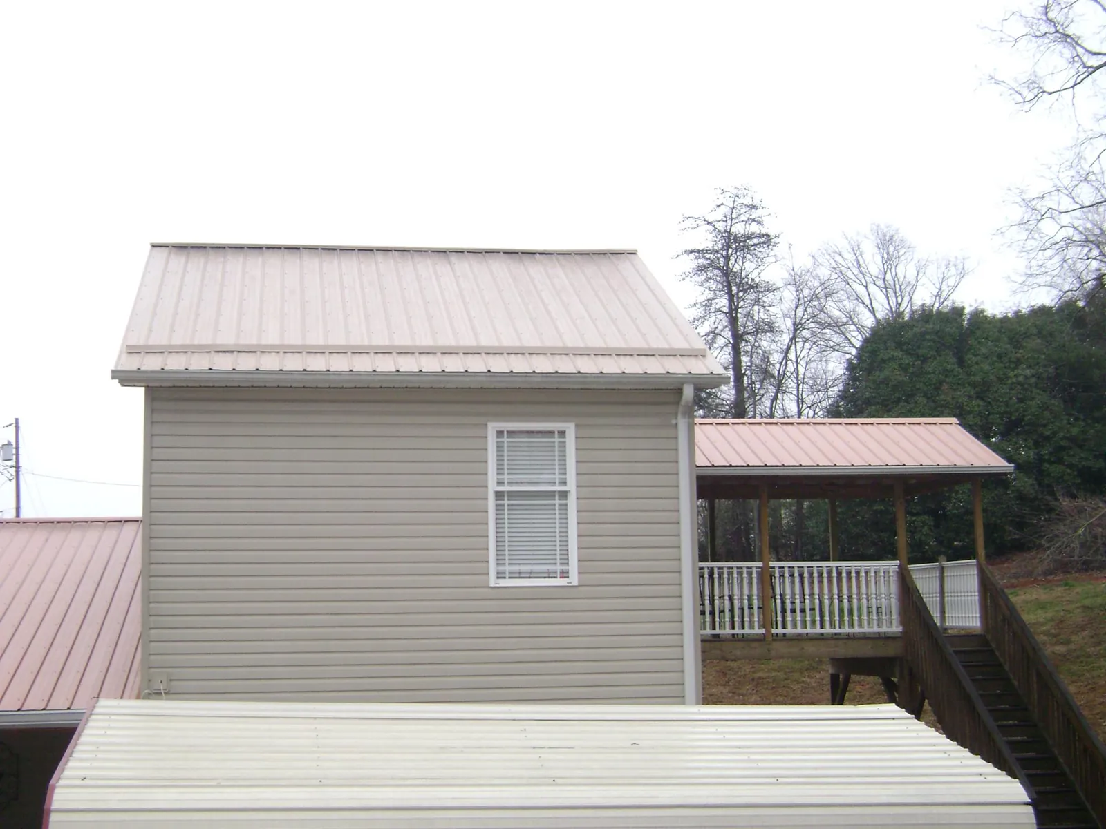 Tan metal roofs on a two story addition and attached porch, from a Roof Replacement job in Fielding